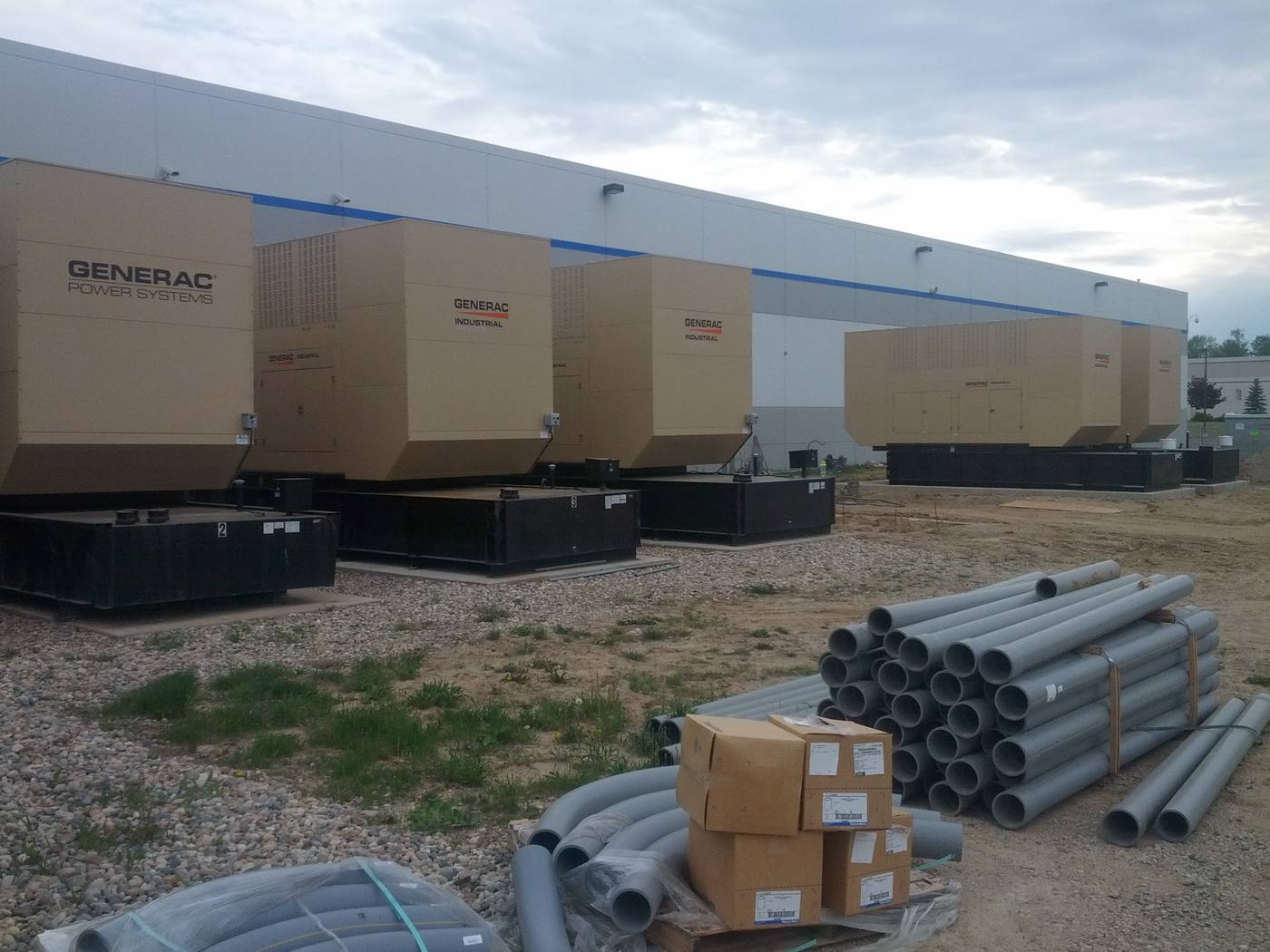A long row of Generac standby generator sets alongside the building, with conduit stacked on the ground.