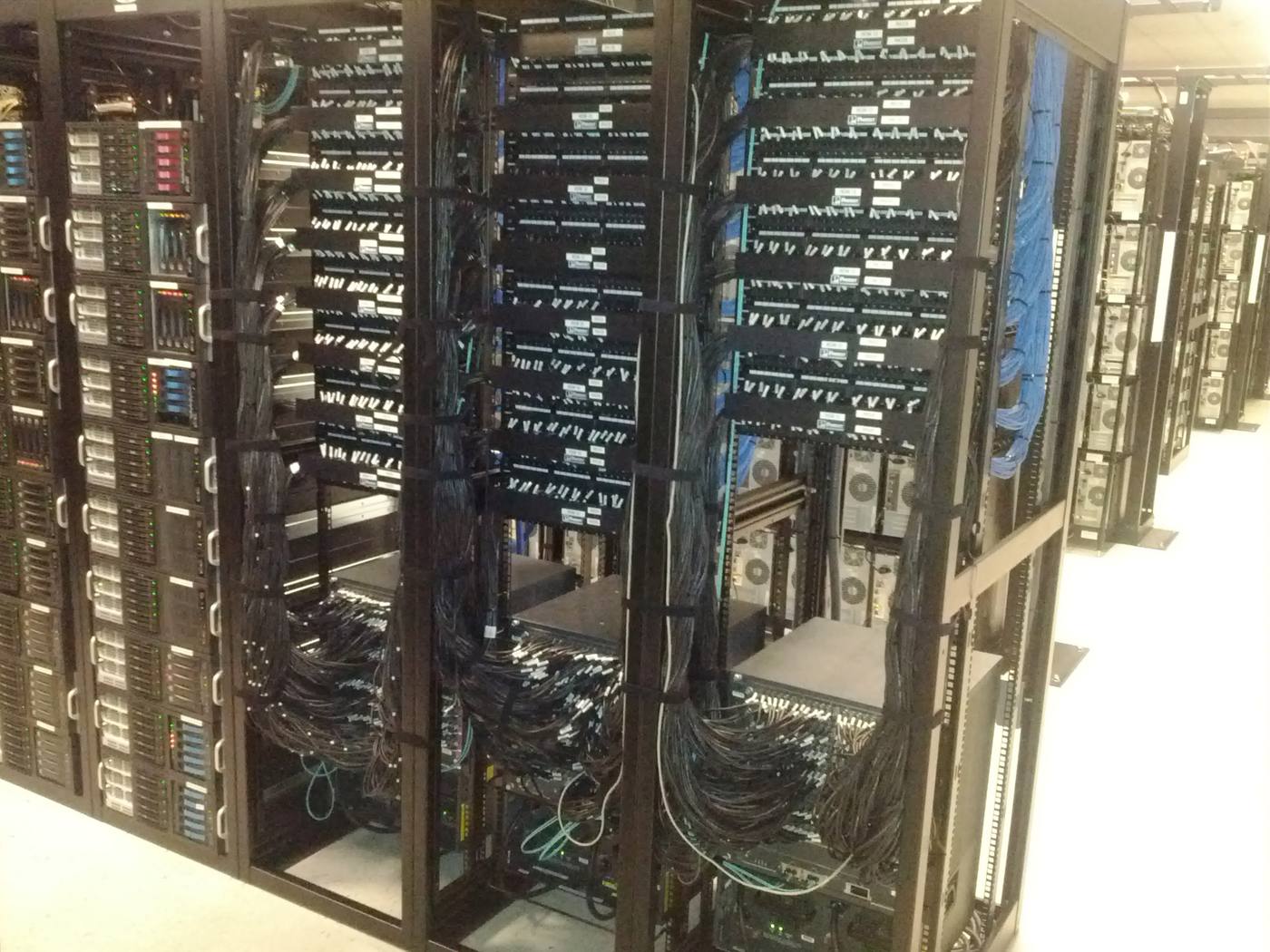 Rows of server racks with dense structured cabling running into vertical managers.