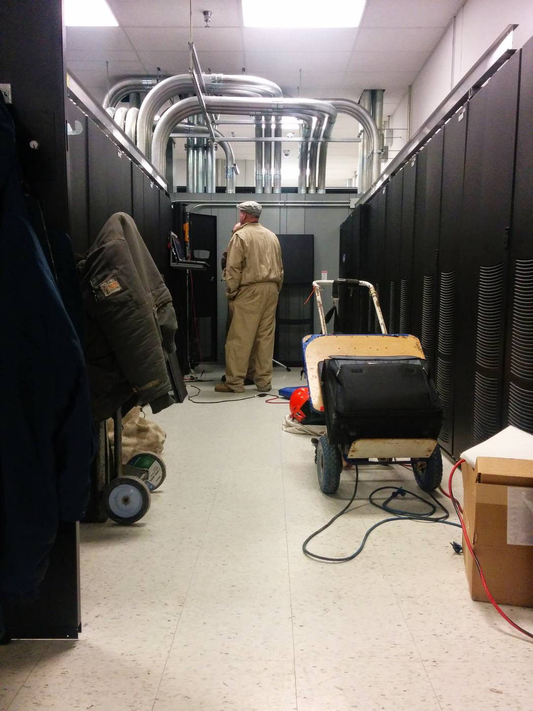 Technicians performing maintenance in the UPS room between rows of cabinets.